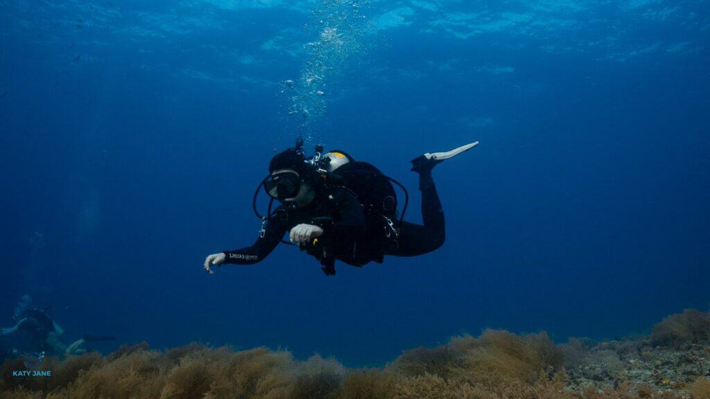 scuba dive floating in blue water blowing bubbles